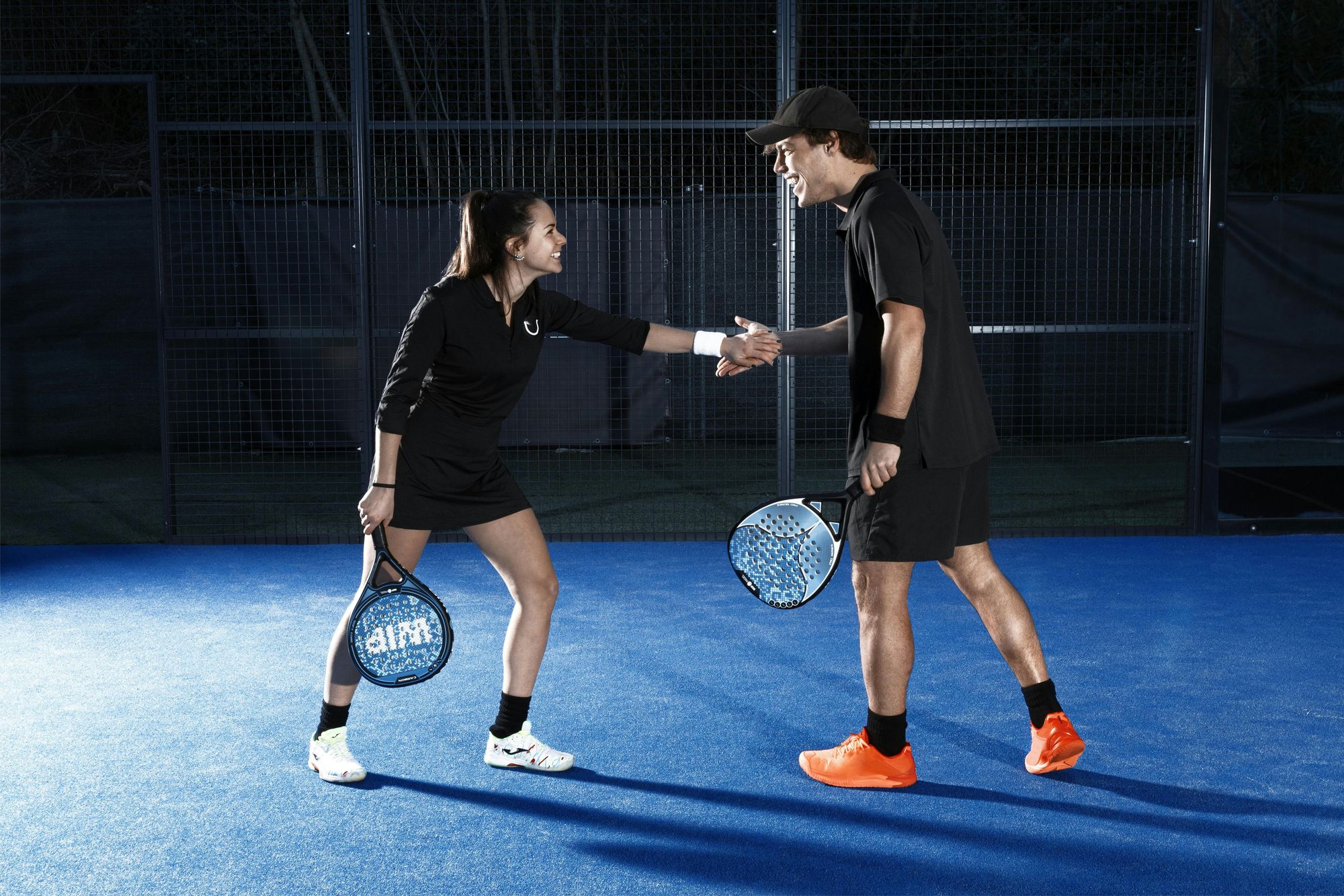 Twee padelspelers in actie op een verlichte padelbaan in de avond