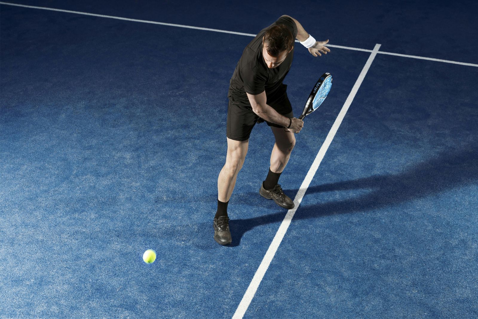 Padelspeler in actiehouding klaar voor een slag op een verlichte baan